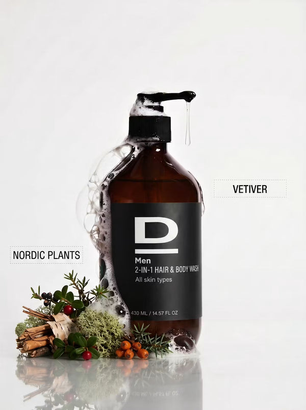 Braune Flasche mit schwarzem Spender und Etikett "D Men 2-IN-1 HAIR & BODY WASH" umgeben von Schaum und Pflanzen mit Beschriftungen "NORDIC PLANTS" und "VETIVER"