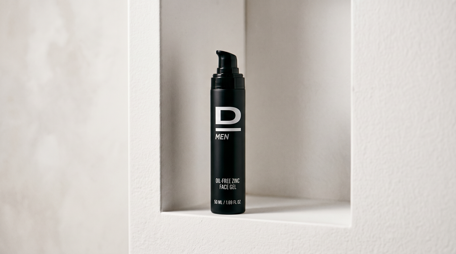 Schwarze Flasche mit Pumpspender und Aufschrift 'D MEN OIL-FREE ZINC FACE GEL' steht in einer rechteckigen Nische in einer hellen Wand