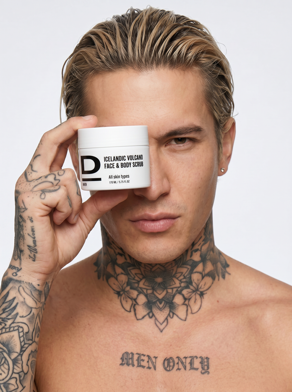 Junger Mann mit Tattoos hält ein weißes Kosmetikgefäß mit der Aufschrift 'ICELANDIC VOLCANIC FACE & BODY SCRUB' vor sein linkes Auge