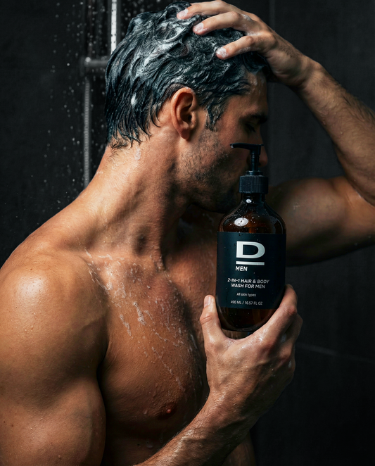 Muskulöser Mann mit nassem Oberkörper hält eine Flasche D MEN 2-IN-1 HAIR & BODY WASH FOR MEN unter der Dusche