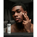 Oberkörper einer Person mit nacktem Oberkörper und Halskette, die sich mit einer Hand das Gesicht berührt, daneben steht ein Flakon mit der Aufschrift 'D MEN HYALURONIC ACID FACE CREAM'.