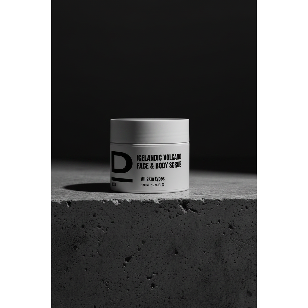 Face & Body Scrub nah. Rundes Kosmetikgefäß mit der Aufschrift 'ICELANDIC VOLCANO FACE & BODY SCRUB' auf rauer Betonoberfläche vor dunklem Hintergrund