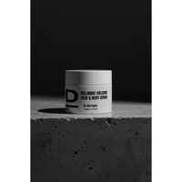 Face & Body Scrub nah. Rundes Kosmetikgefäß mit der Aufschrift 'ICELANDIC VOLCANO FACE & BODY SCRUB' auf rauer Betonoberfläche vor dunklem Hintergrund