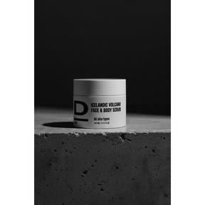 Face & Body Scrub nah. Rundes Kosmetikgefäß mit der Aufschrift 'ICELANDIC VOLCANO FACE & BODY SCRUB' auf rauer Betonoberfläche vor dunklem Hintergrund