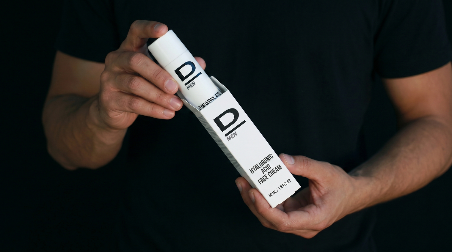 Hände halten eine weiße Verpackung mit der Aufschrift 'D MENS' und 'HYALURONIC FACE CREAM'