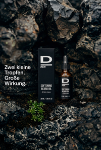 Flasche und Verpackung von D MEN Softening Beard Oil auf dunklem, rauem Gestein mit kleinem grünen Pflänzchen und Text 'Zwei kleine Tropfen, Große Wirkung'
