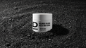 Weißer Tiegel mit schwarzer Aufschrift 'ICELANDIC VOLCANO FACE & BODY SCRUB' steht auf schwarzem, körnigem Vulkanboden