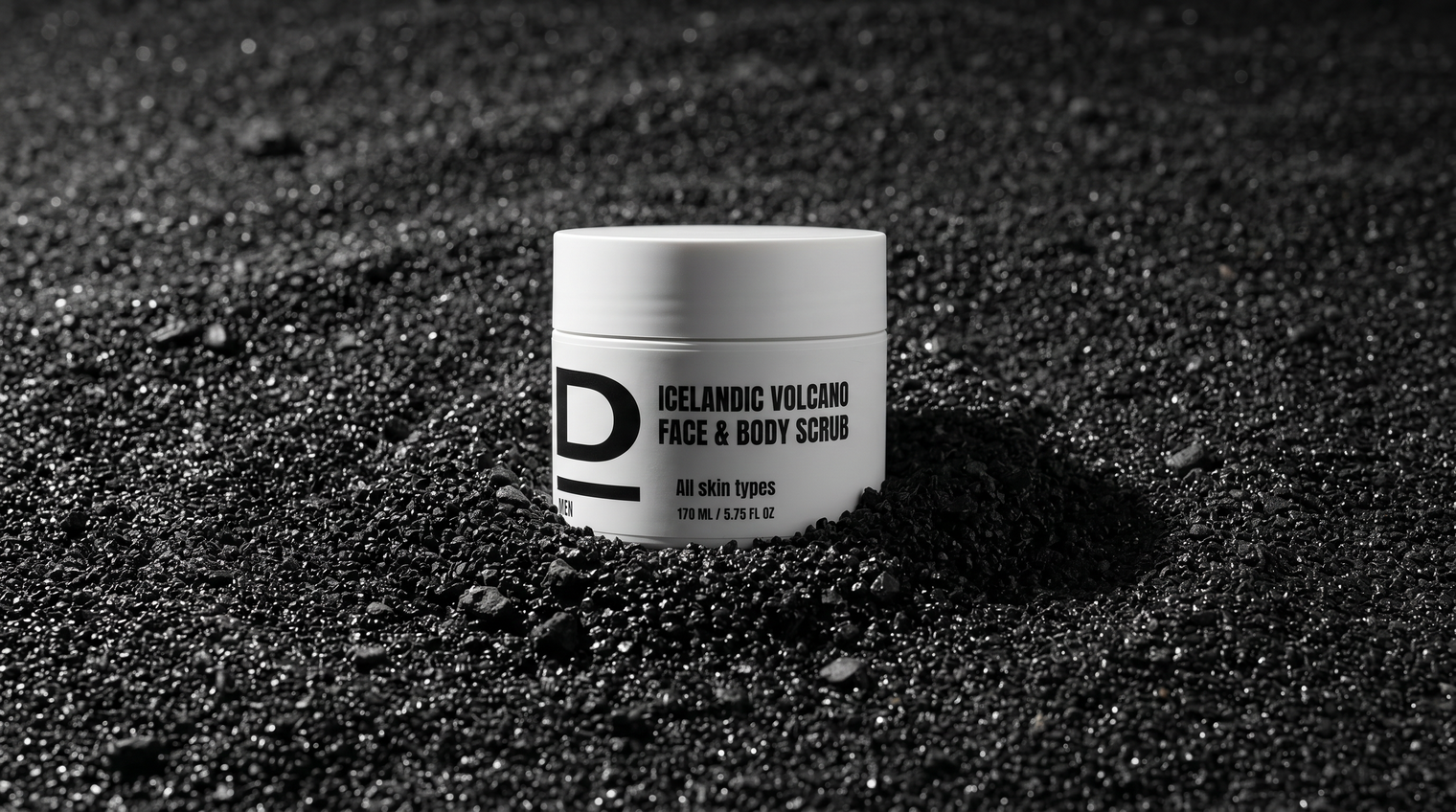 Weißer Tiegel mit schwarzer Aufschrift 'ICELANDIC VOLCANO FACE & BODY SCRUB' steht auf schwarzem, körnigem Vulkanboden