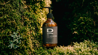 Braune Flasche mit Pumpspender und Etikett vor grünem Moos und Pflanzen